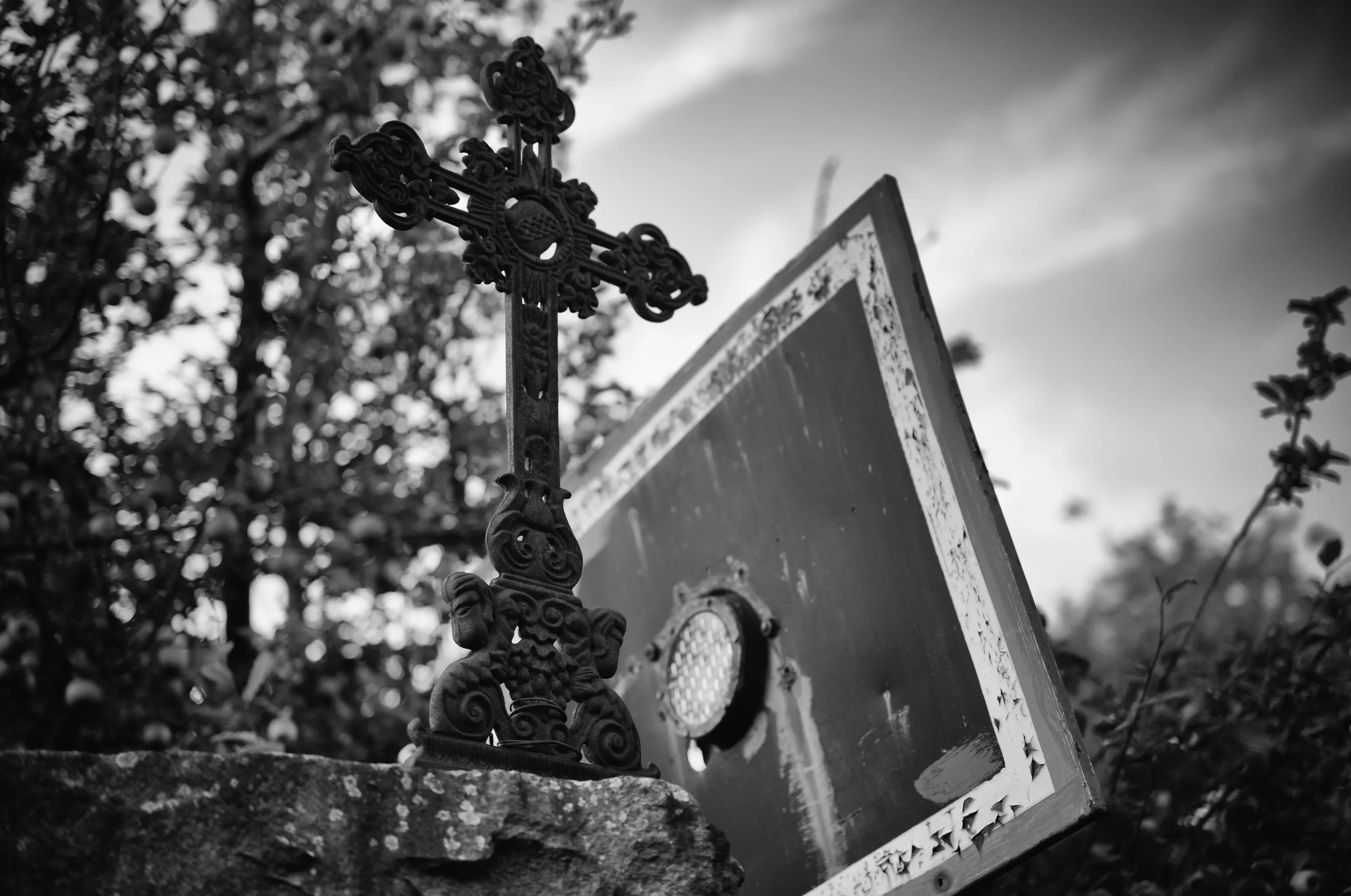 Schmiedeeisernes Kreuz neben einem schiefen Schild