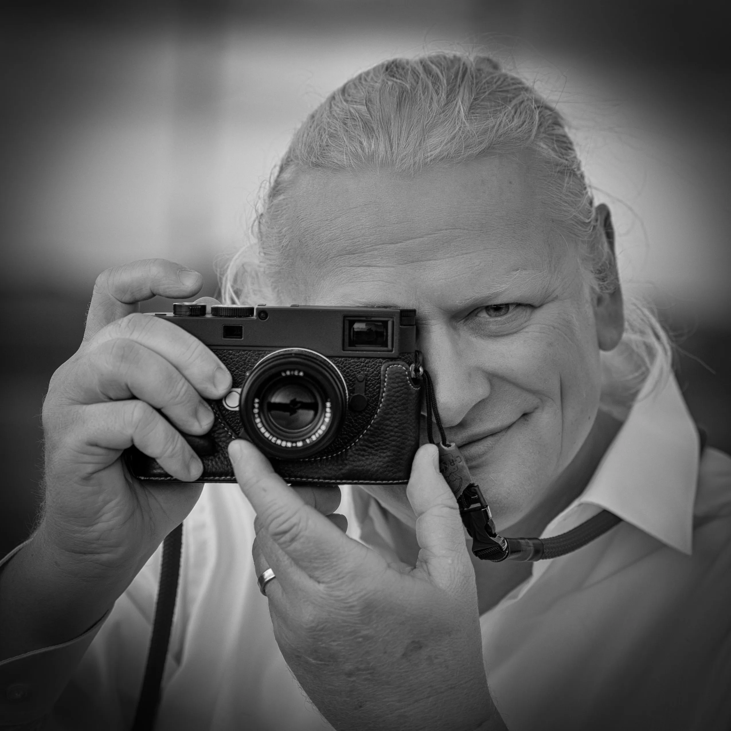 Franz Paul Podek blickt lächelnd durch den Sucher seiner Leica